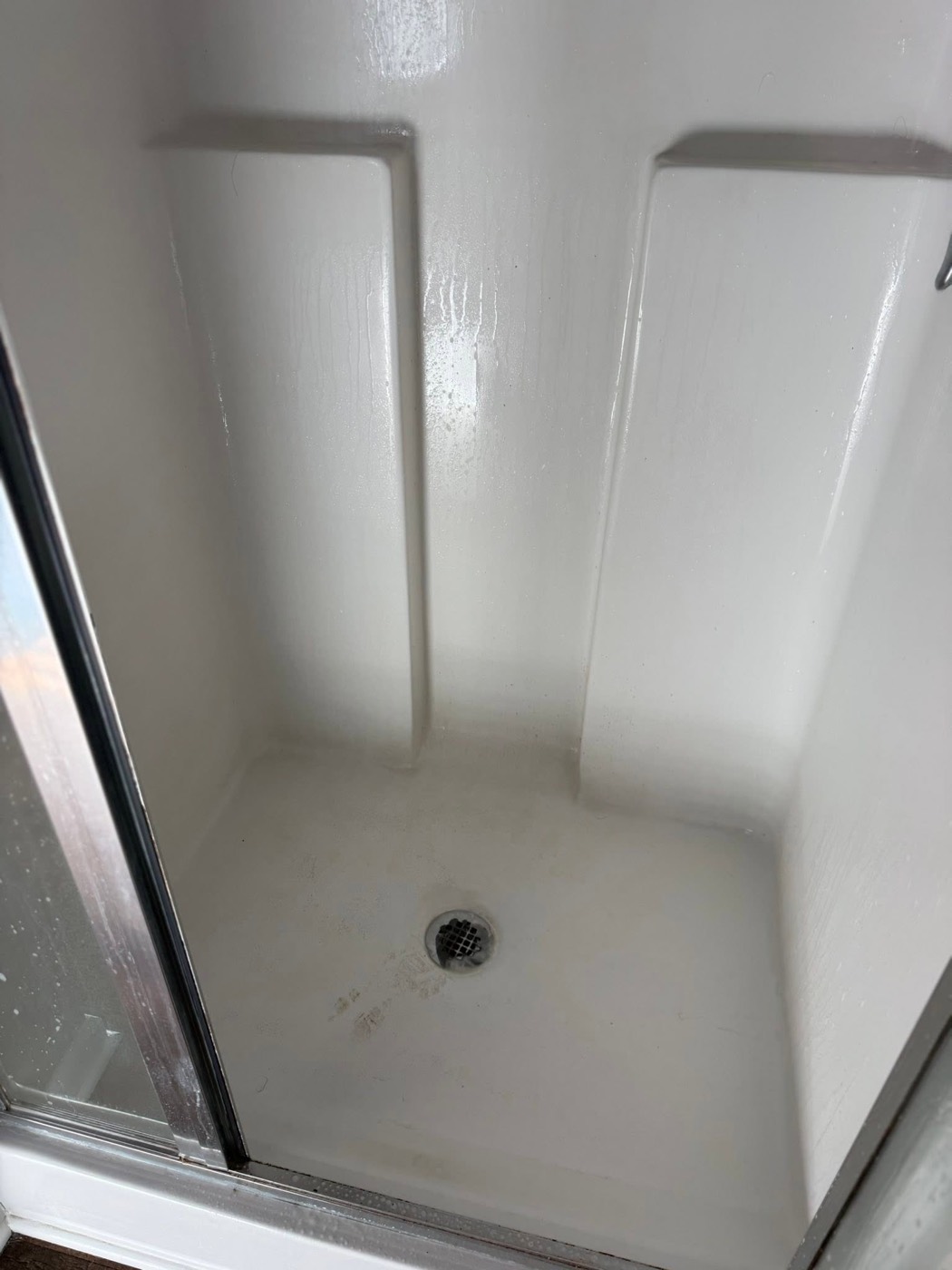 Shower stall before cleaning, water spots on the glass and staining on the floor